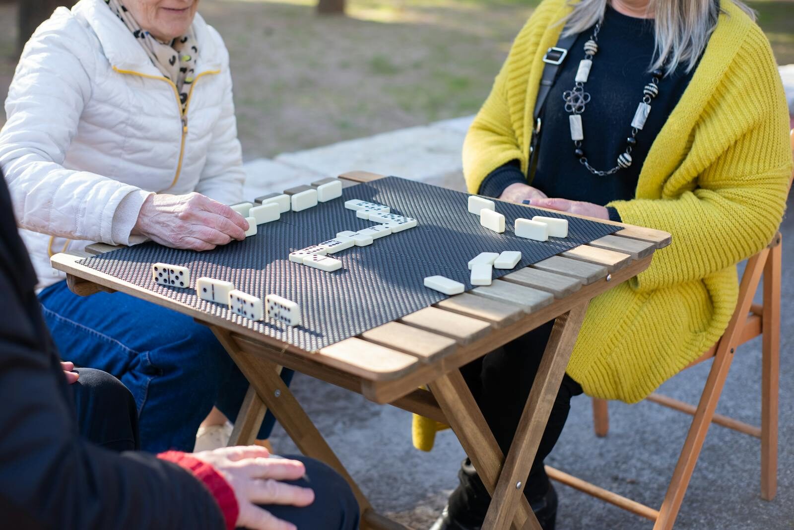 Senior adults playing dominoes at an outdoor table, enjoying leisure time.