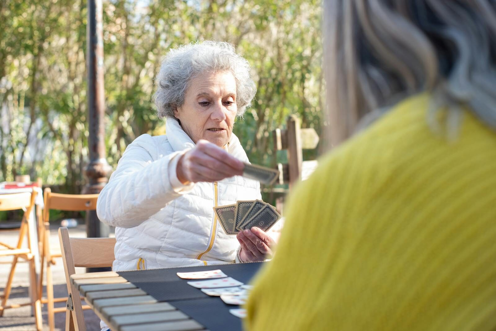 Two senior women enjoying a card game outside in Portugal on a sunny day.